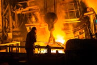 一名工人在工厂里操作机器，使用熔融金属和强烈的火焰