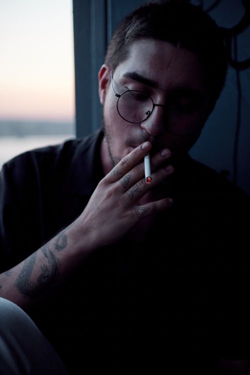 Free A man smoking a cigarette at dusk with a tattooed arm, set against the backdrop of Istanbul scenery. Stock Photo