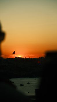 A stunning cityscape with a national flag silhouetted against a vibrant sunset over water.