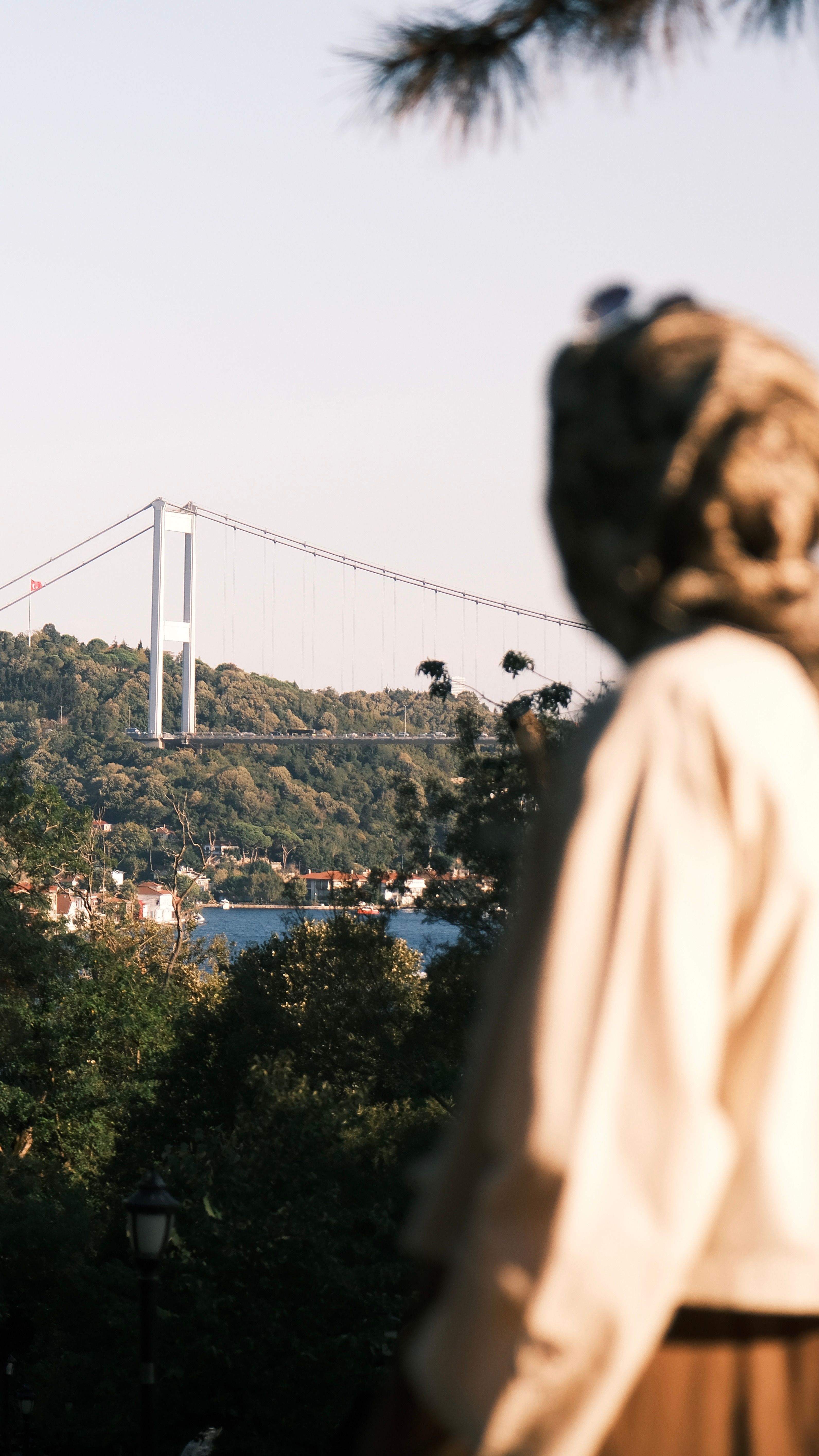 A woman in a hijab gazes at the Bosphorus Bridge on a sunny summer day.