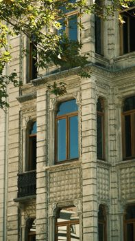 Detailed view of a historic stone building facade with ornate windows and lush foliage reflecting sunlight.
