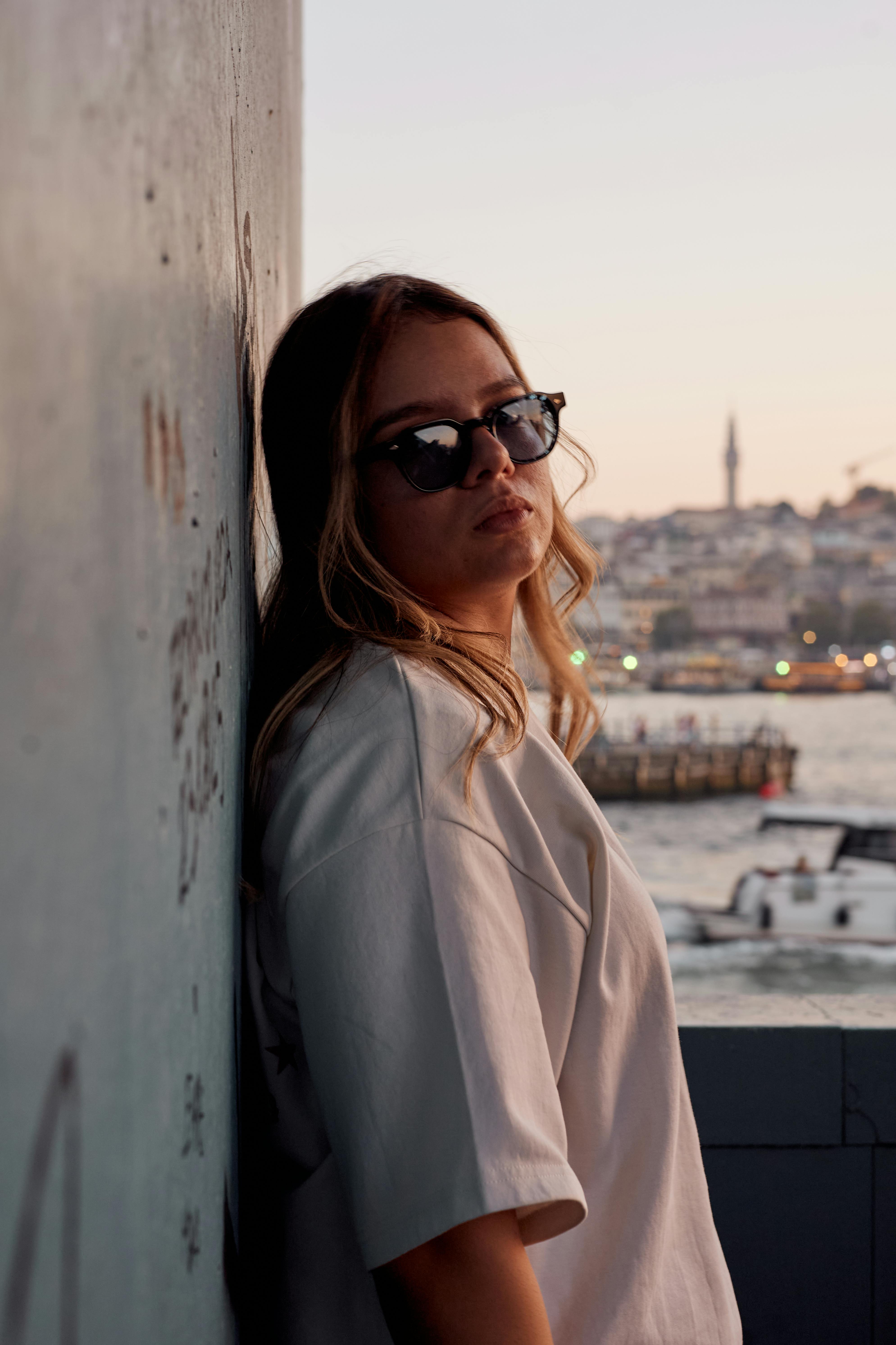Stylish woman in sunglasses stands by Istanbul's scenic waterfront during sunset.