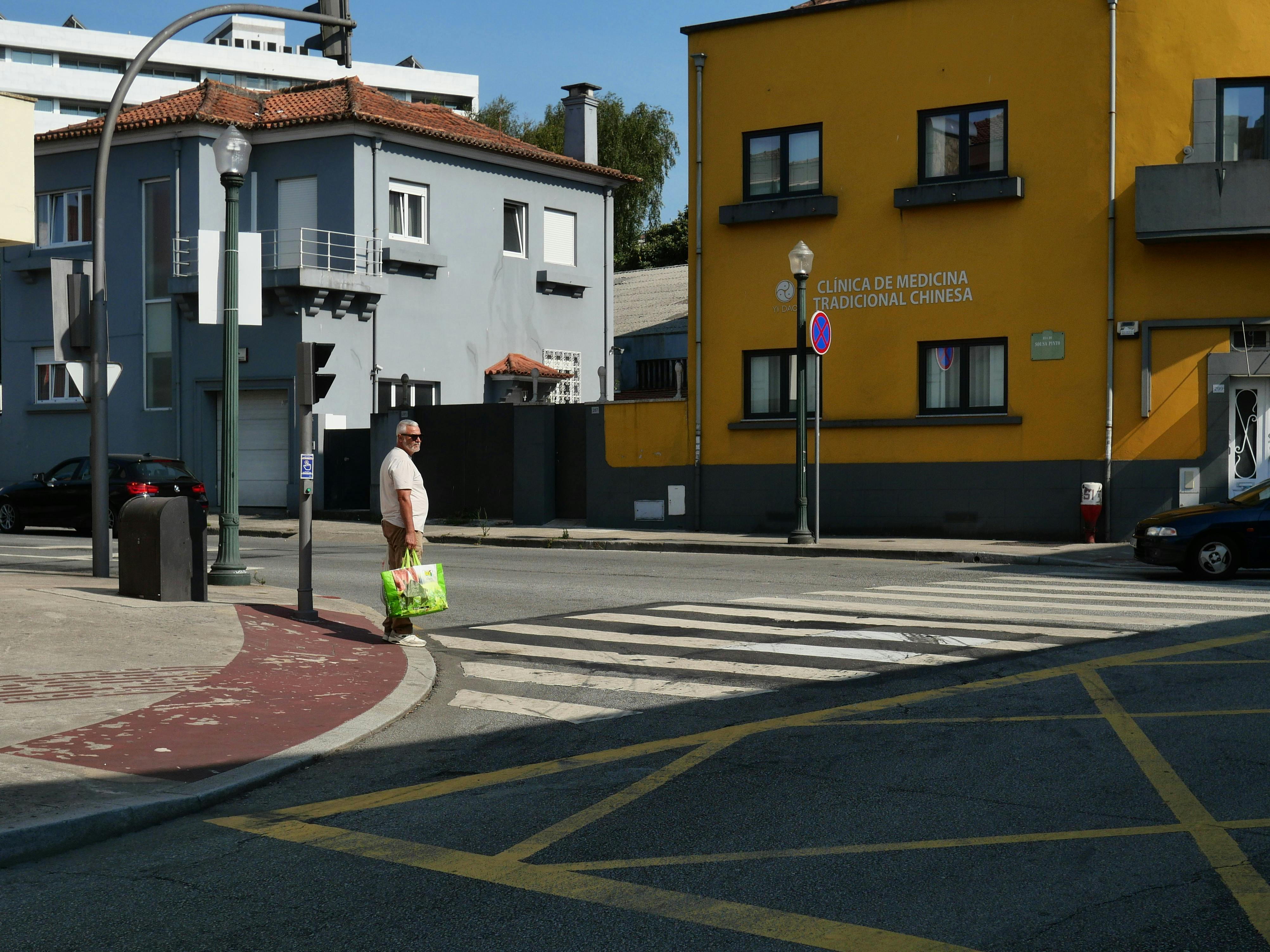 A man crossing the street near a traditional Chinese medicine clinic on a sunny day.