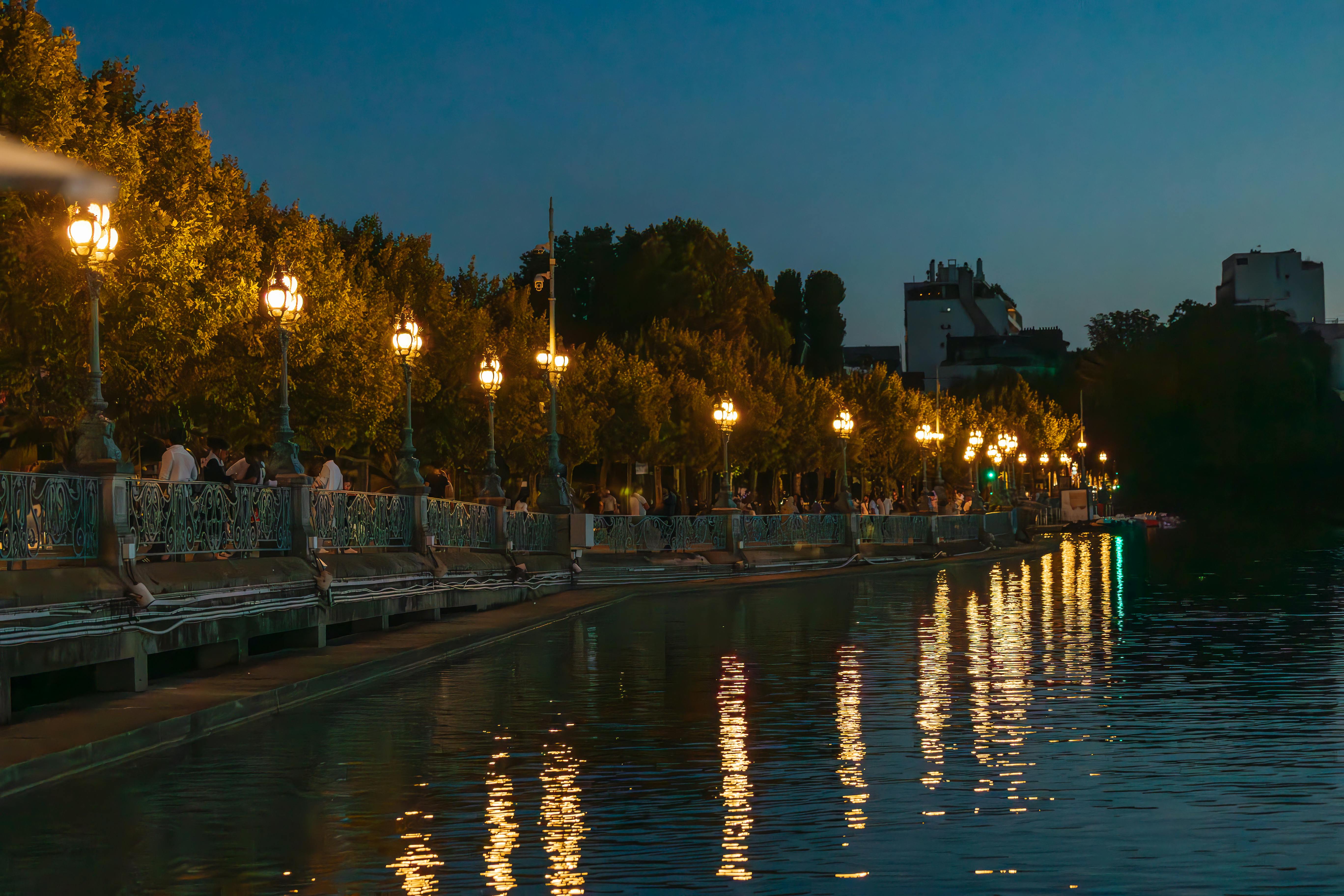Peaceful evening scene of Paris canal with lit street lamps and reflections on water.
