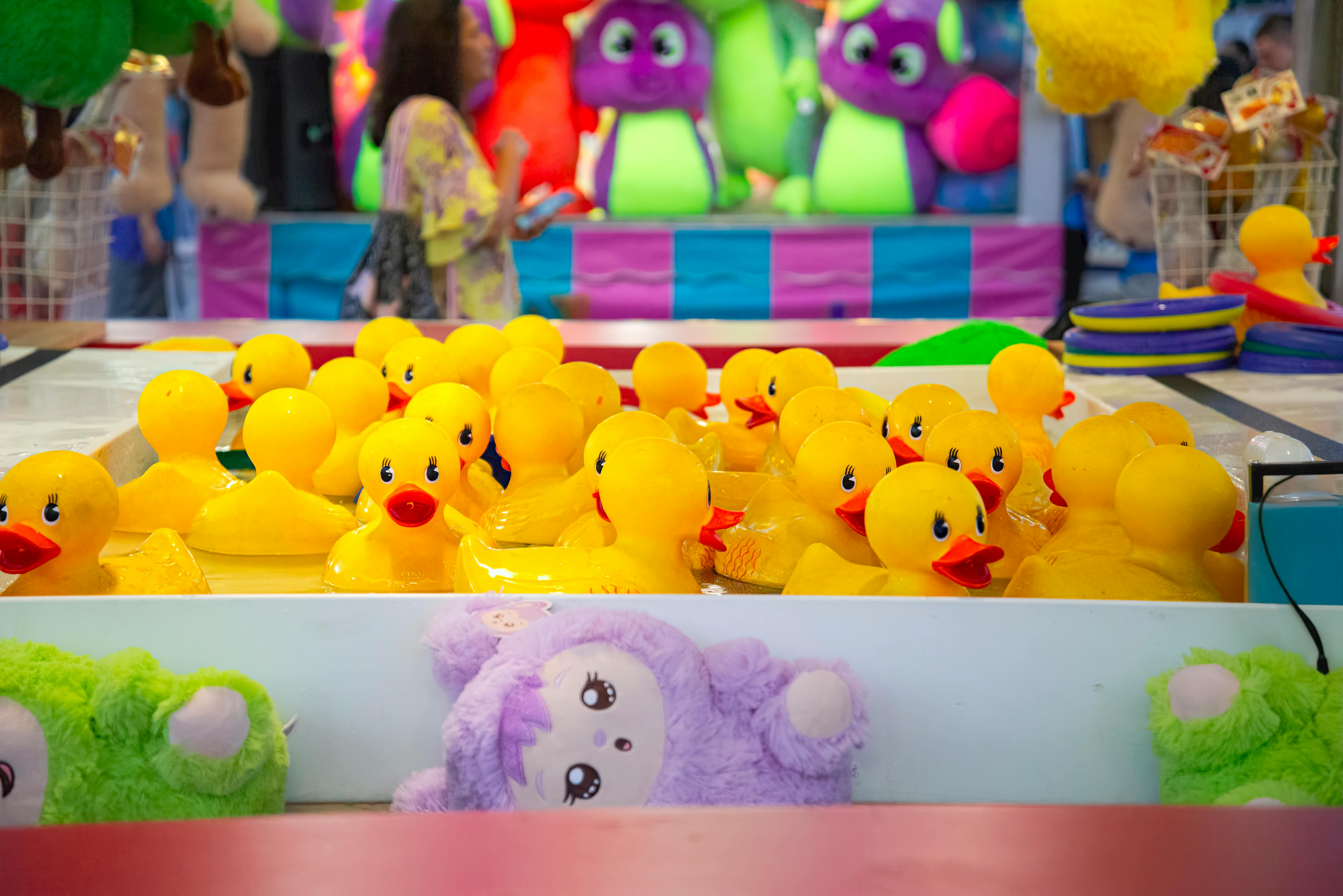 Colorful carnival game with yellow rubber ducks and vibrant plush toys in the background.