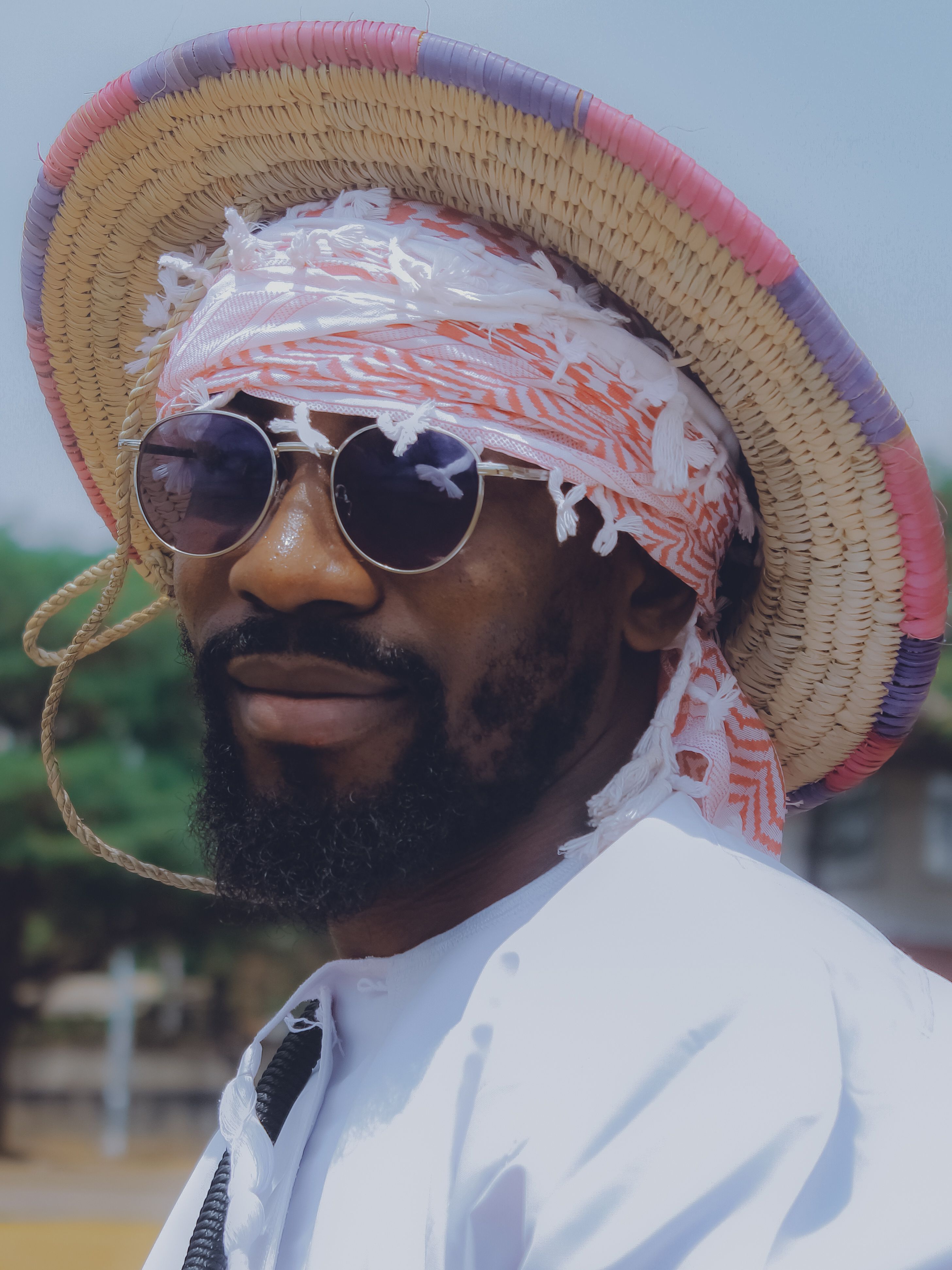 Stylish portrait of a man in traditional attire and straw hat outdoors.