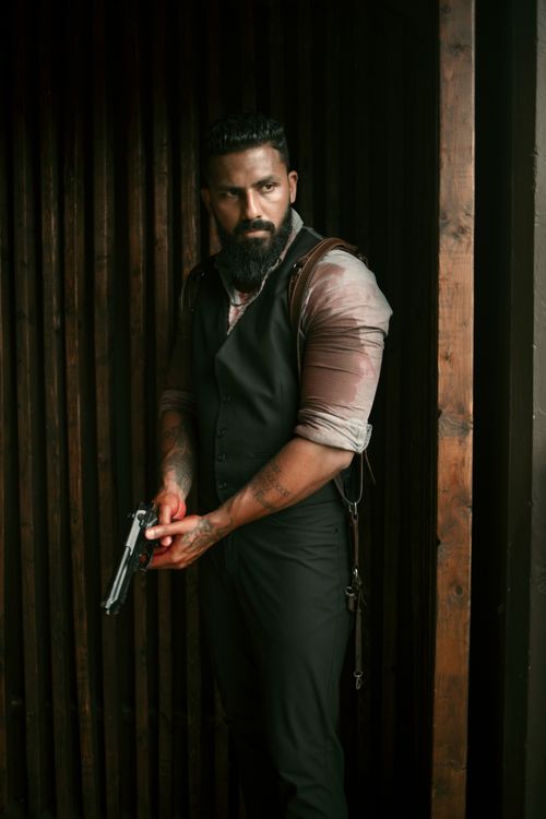 Free Intense portrait of a man with a gun in a dark, moody setting wearing a black suit. Stock Photo
