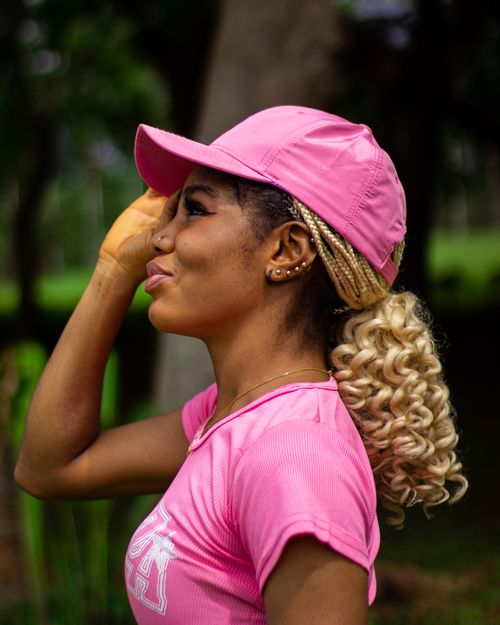 Free Portrait of a young woman wearing a pink cap and top, smiling in an outdoor setting. Stock Photo