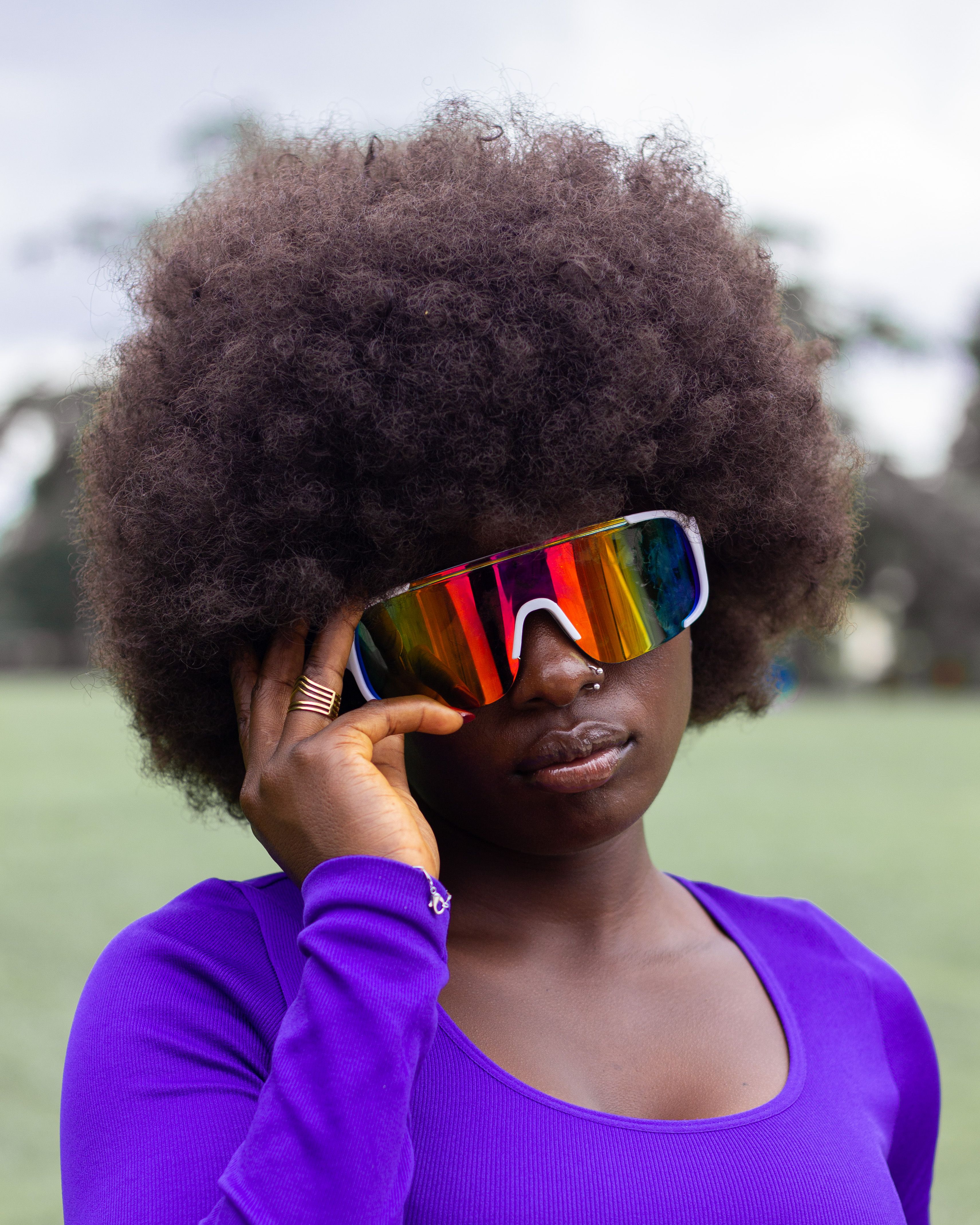 Fashionable woman with afro hairstyle wearing rainbow sunglasses outdoors. Vibrant and modern look.