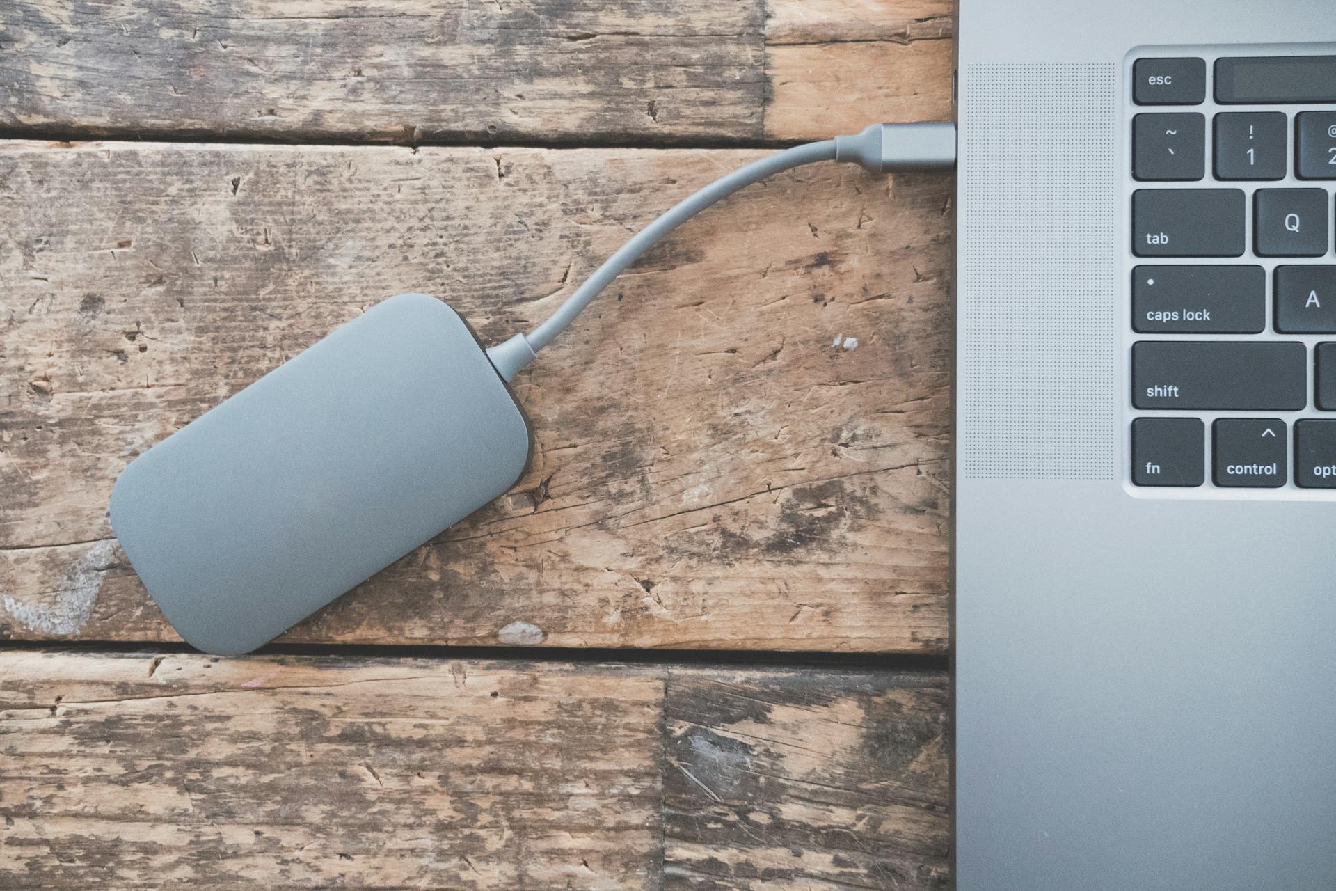 Close-up of an external hard drive connected to a laptop on a rustic wooden table.