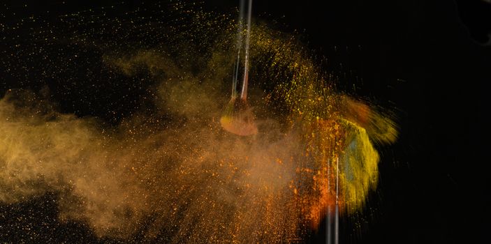 A vivid explosion of makeup powder captured around a makeup brush on a dark background.