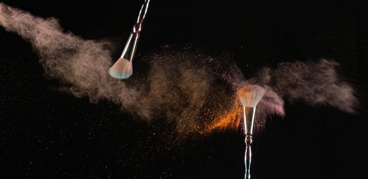 Close-up of makeup brushes releasing vibrant powder against a black background.