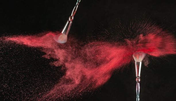 Vibrant explosion of red makeup powder captured with motion from two brushes on a dark background.
