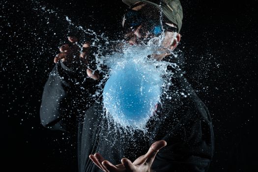 A water balloon bursts in dramatic fashion, capturing the splash mid-air against a dark background.