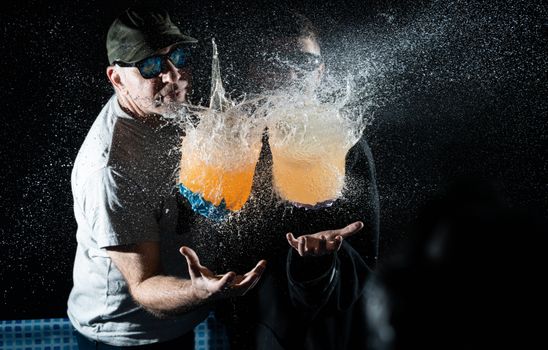 Two men capture an intense water balloon burst, frozen in motion.