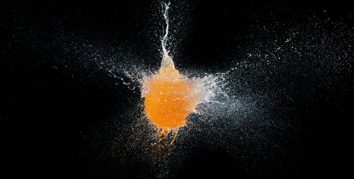 Stunning capture of orange paint explosion with splash effect and contrast against black background.