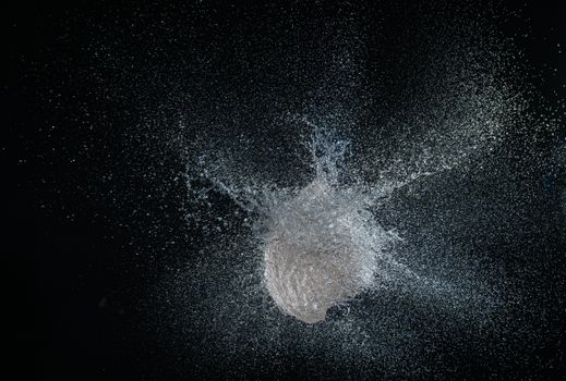 High-speed capture of a water balloon exploding with water droplets against a dark background.