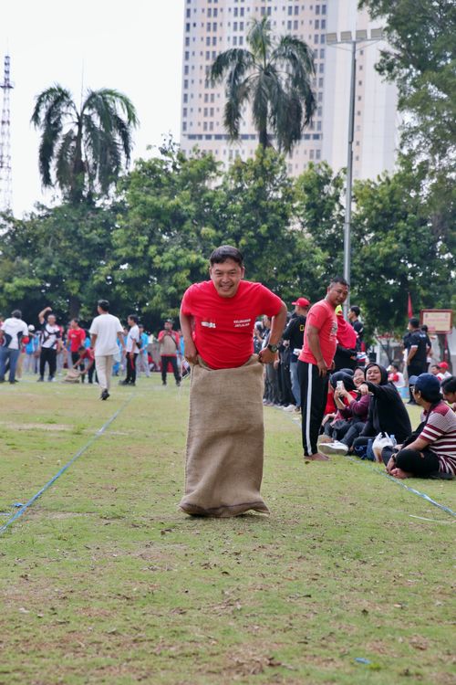 Free Man participating in a lively sack race during a community event in a city park. Stock Photo