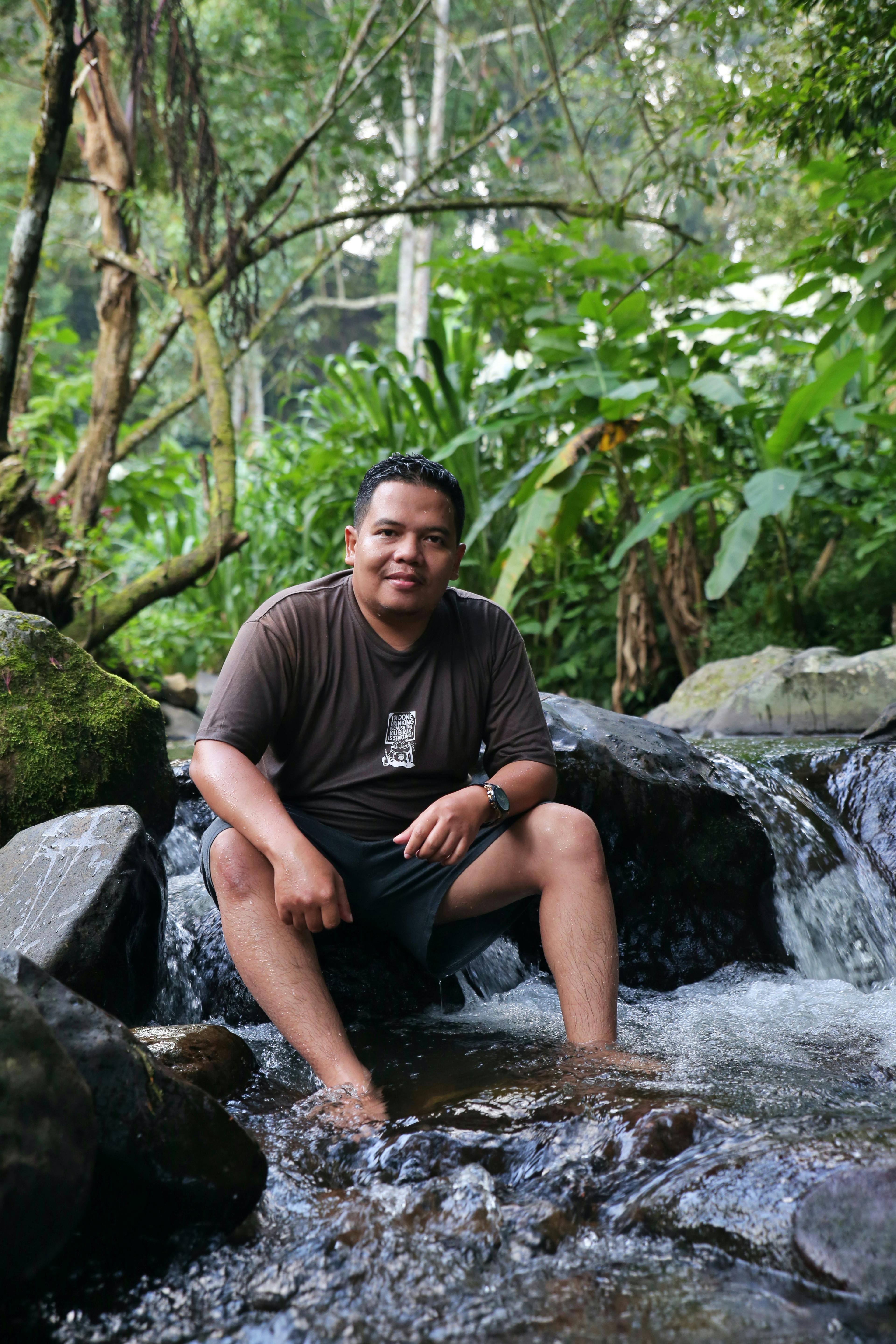 An adult male sitting in a forest stream, enjoying nature's tranquility.