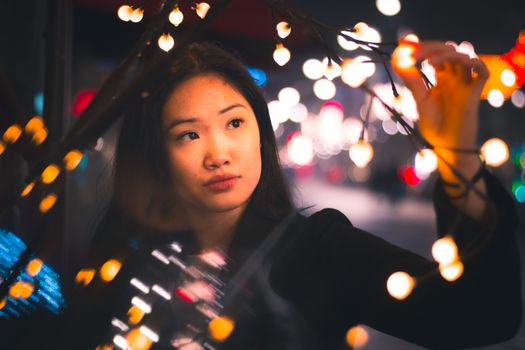 A young woman observes string lights at night in Lahti, Finland, creating a festive mood with bokeh lighting.