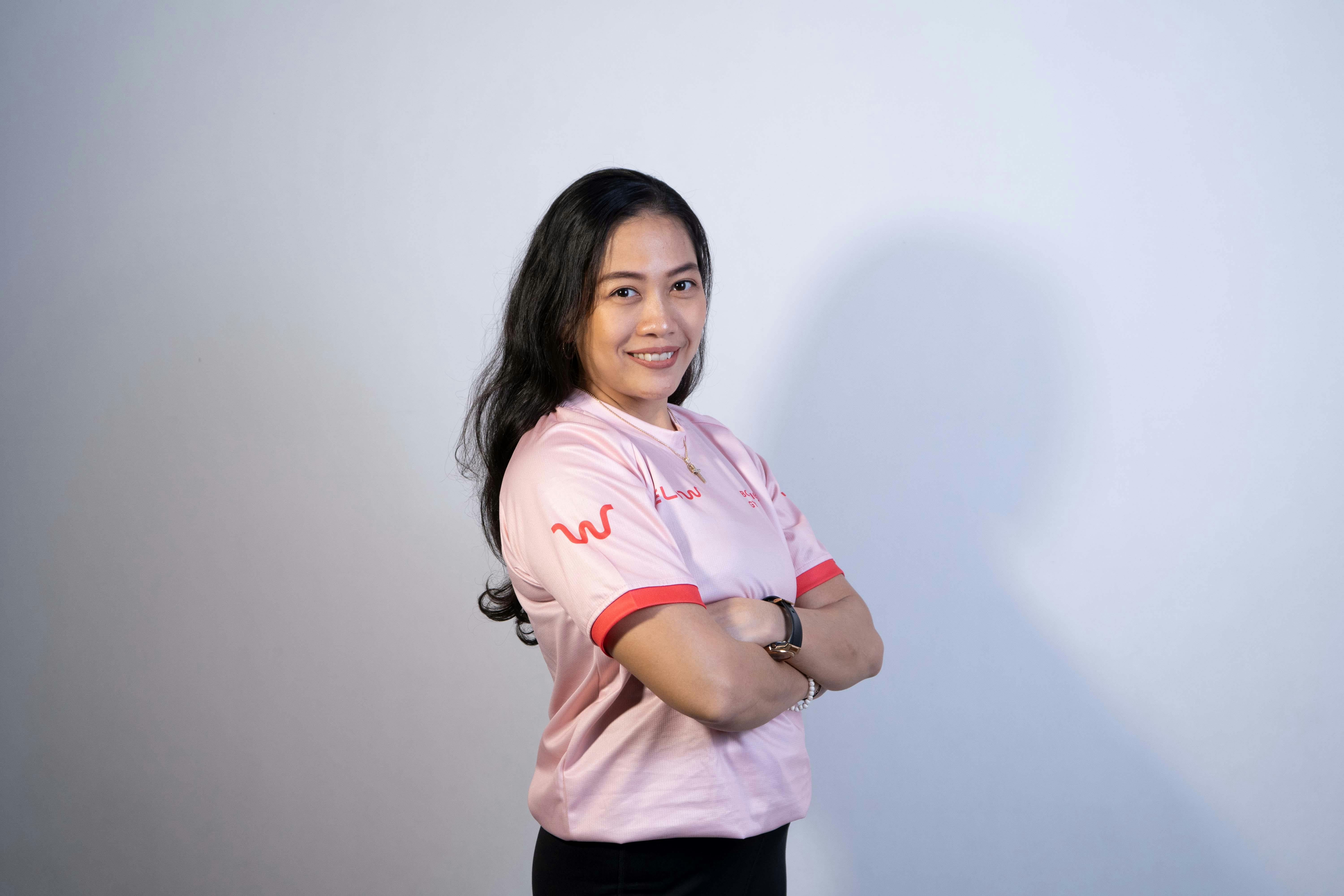 Portrait of a smiling Asian woman in a pink shirt with arms crossed, exuding confidence.