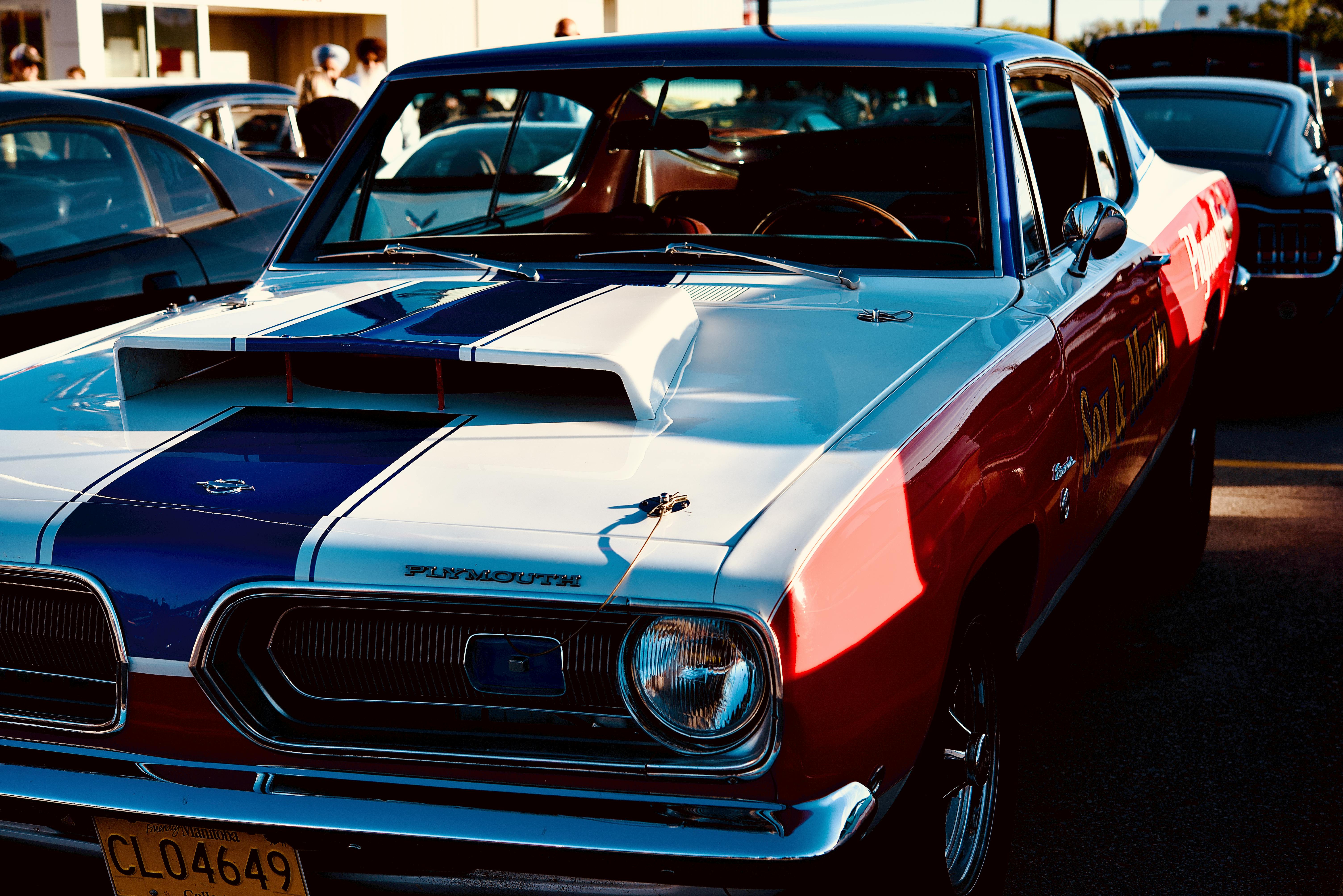 Close-up of a classic red and white Plymouth coupe at an outdoor car show in bright sunlight.