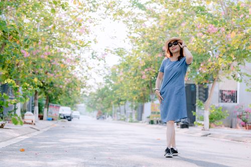 Free Woman in blue dress and hat walking down a sunny, flower-lined street. Stock Photo