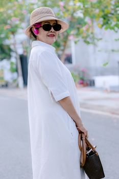 Elegant senior woman in sunglasses and hat smiling outdoors in summer.