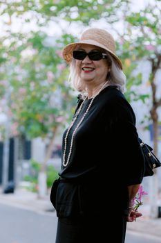 Elegant senior woman in sunglasses and hat smiling in a sunny outdoor setting.