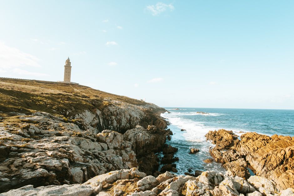 A scenic lighthouse standing on a rugged cliffside by the ocean under a clear blue sky.