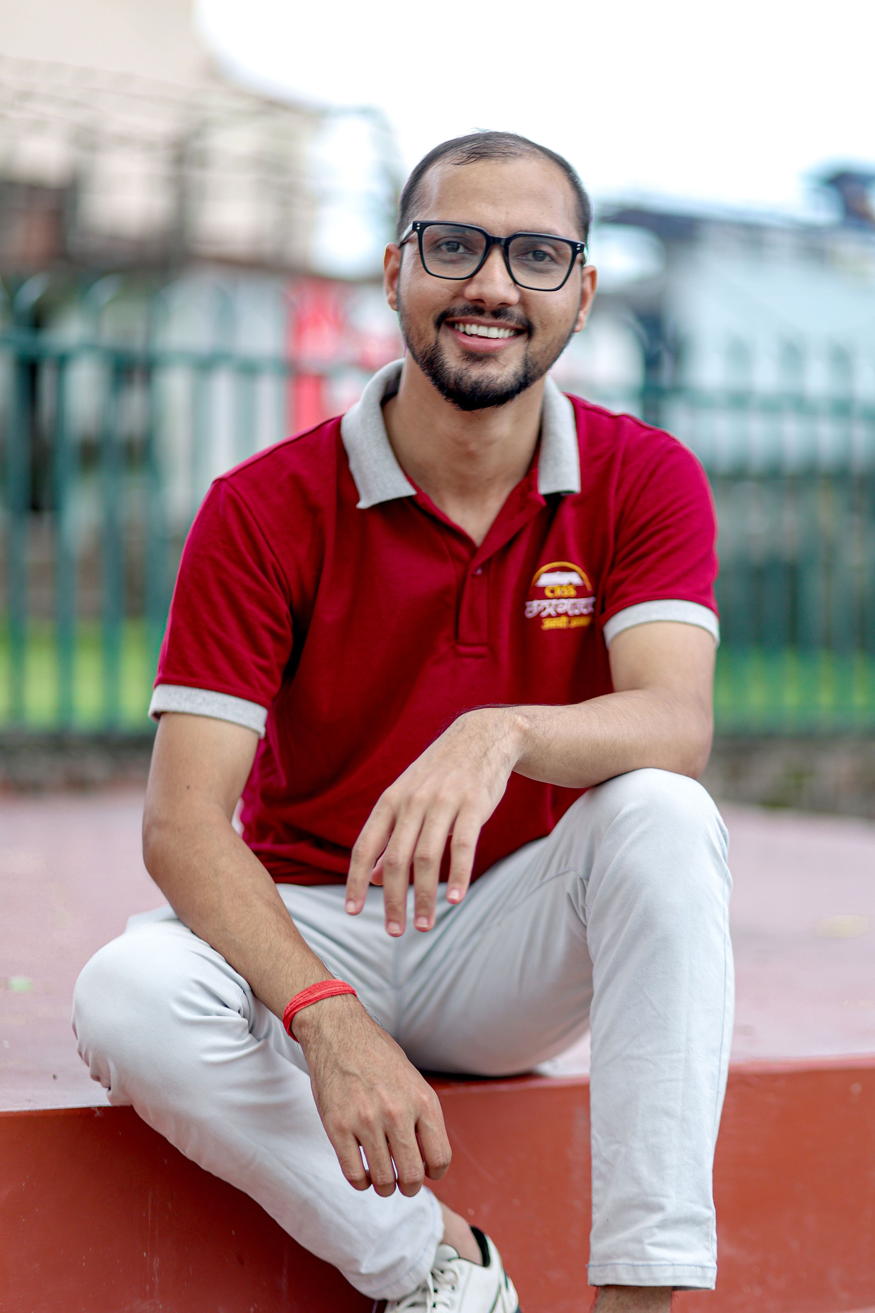 Smiling man seated outdoors in a red polo, exuding a friendly and approachable vibe.