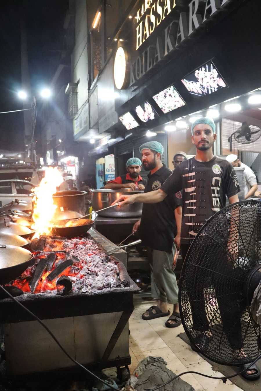 Cooks preparing karahi over open flames at night