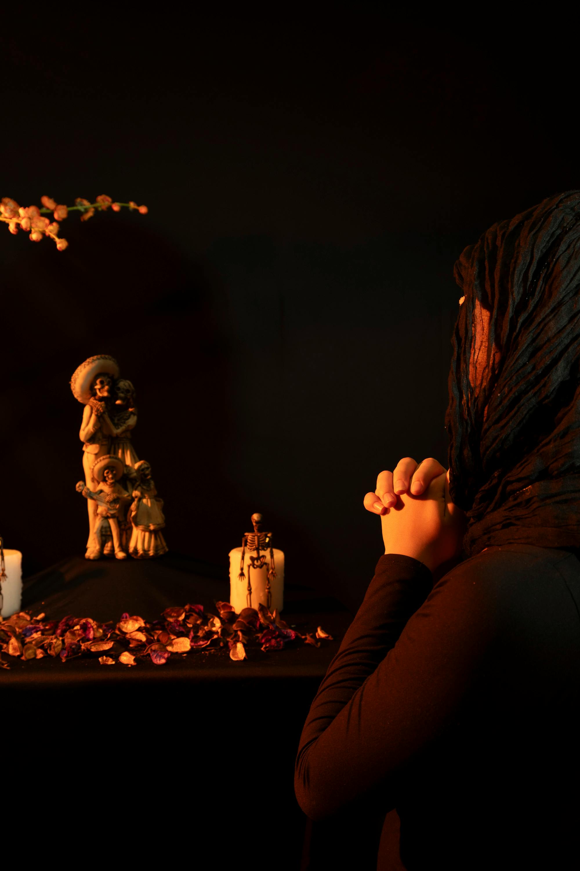 Gratis Una mujer en oración en un altar del Día de Muertos con estatuas, velas y pétalos, creando una atmósfera solemne. Foto de stock