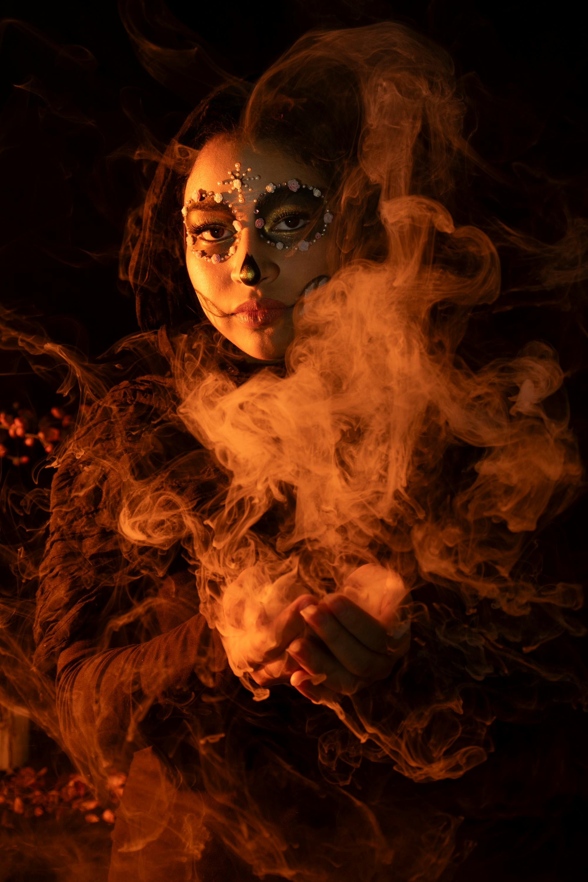 Gratis Ritratto di una donna truccata per il Dia de los Muertos, circondata dal fumo, che crea un'atmosfera enigmatica. Foto a disposizione