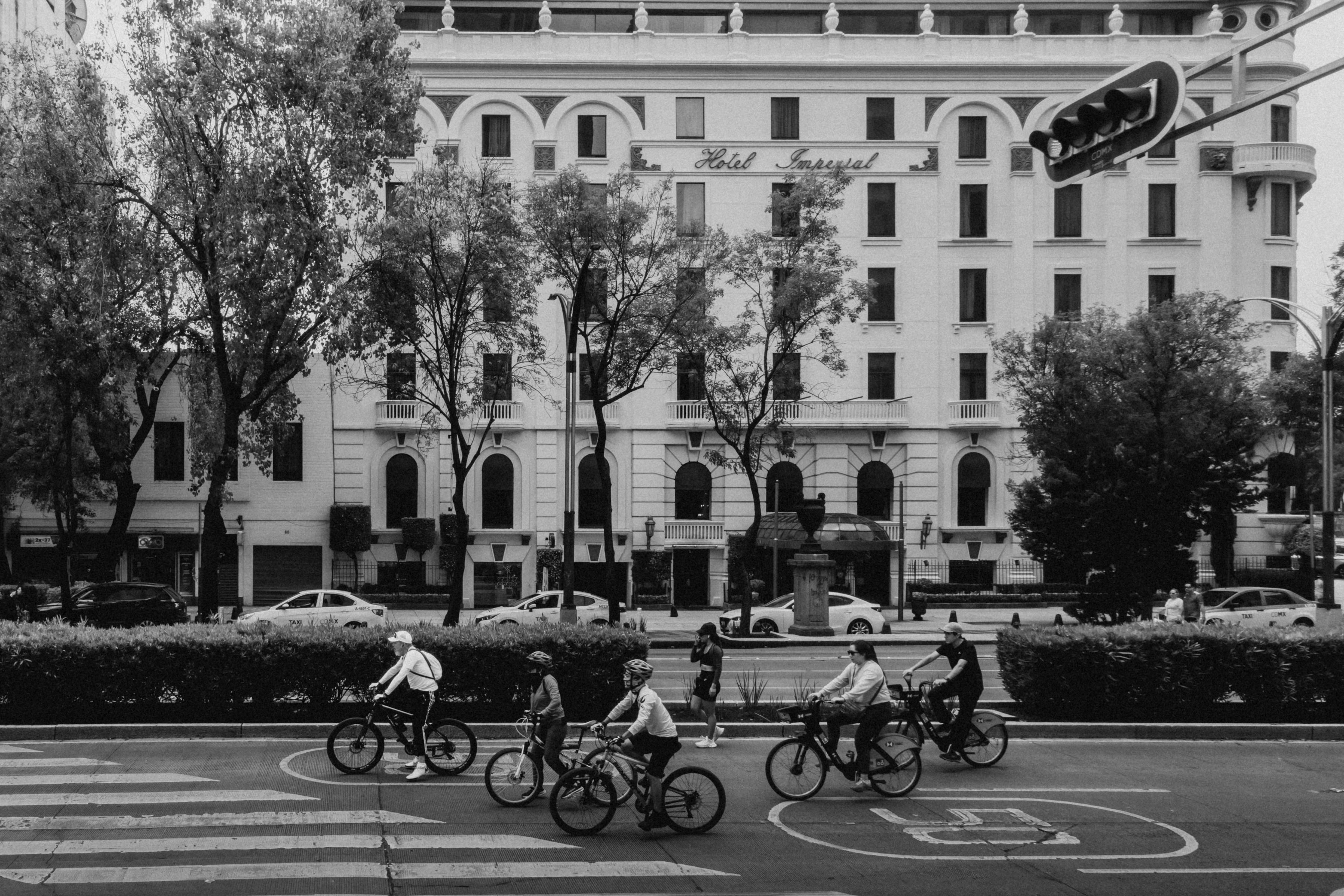 A group of cyclists biking past Hotel Imperial in Mexico City on a lively day.