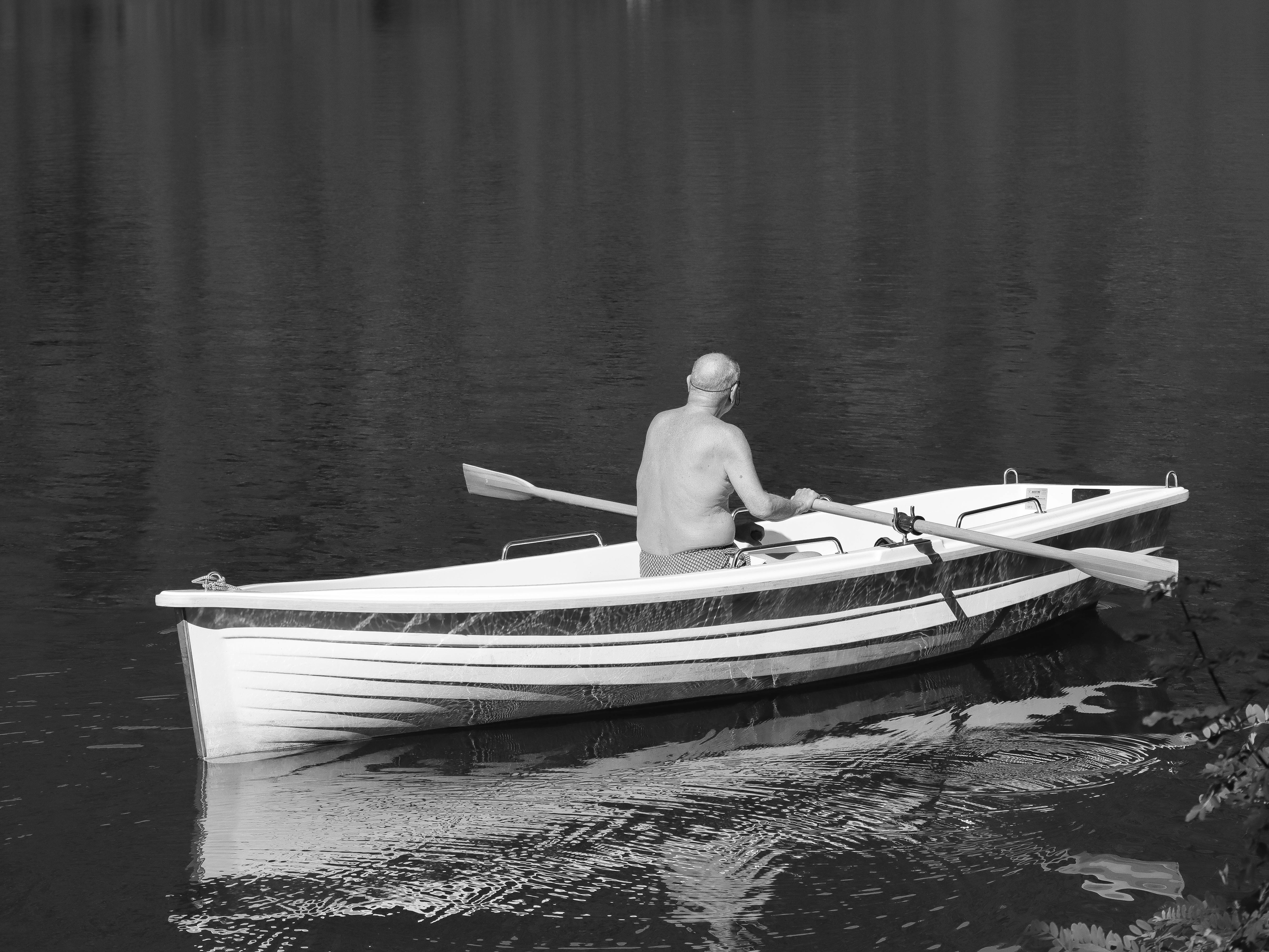 Black and white photo of an elderly man rowing a boat on calm water, peaceful scene.