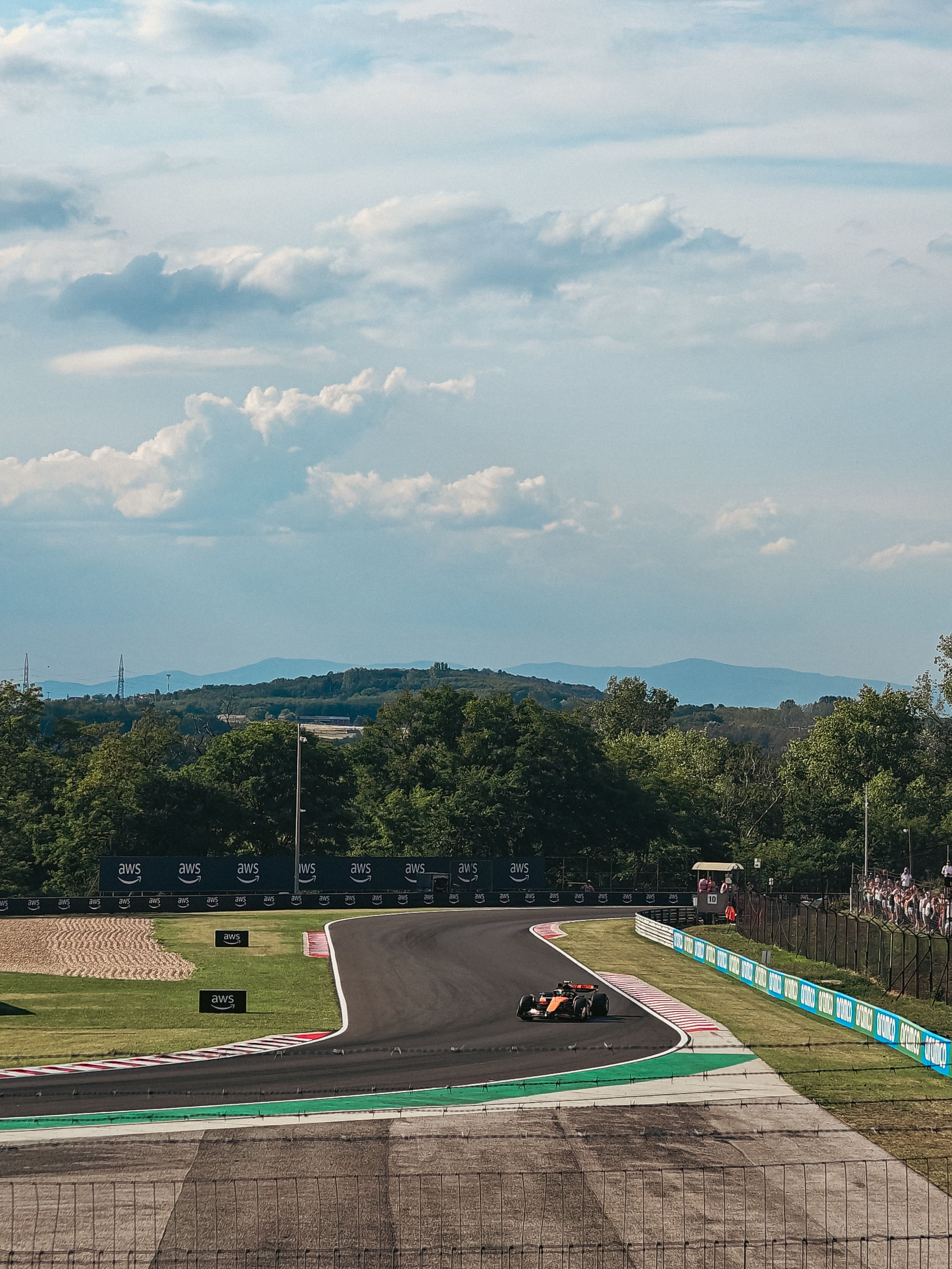 Een Formule 1-racewagen raast over de baan, omgeven door weelderig groen landschap en toeschouwers onder een zonnige hemel.