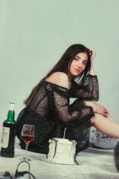 Woman in a stylish black dress celebrating a birthday with cake and wine in a studio setting.