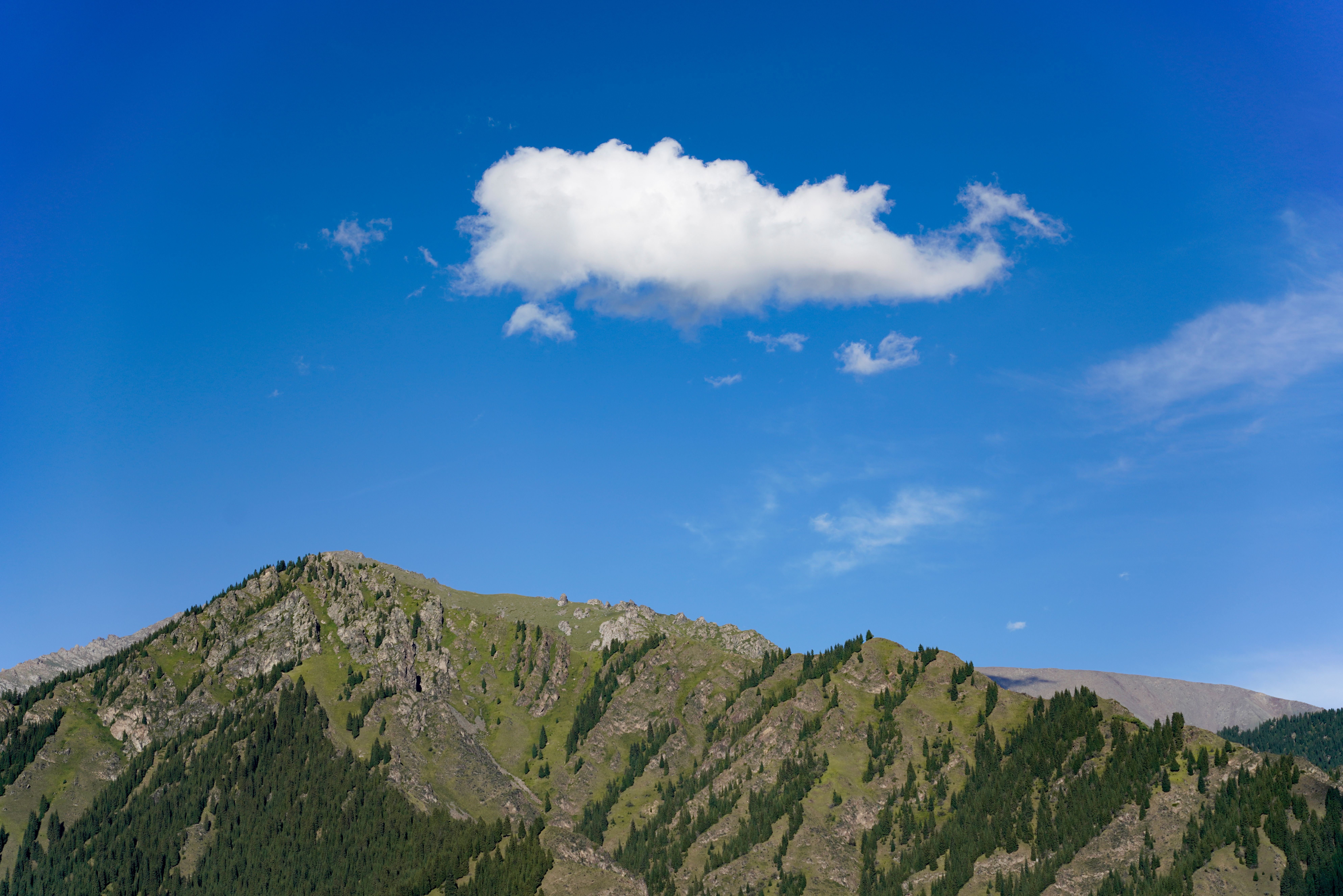 Serene mountain scene with a lone cloud in a clear blue sky.