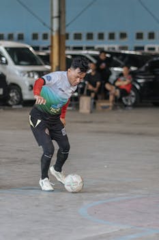 A soccer player skillfully dribbling a ball indoors with cars in the background.