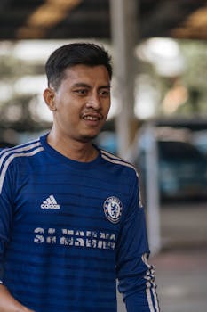 Smiling man wearing a blue sports jersey outdoors, under overhang