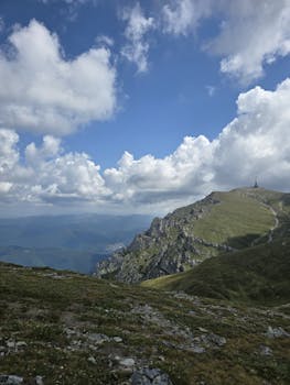 Stunning mountain landscape with a visible pathway leading to a summit, under a sky filled with clouds.