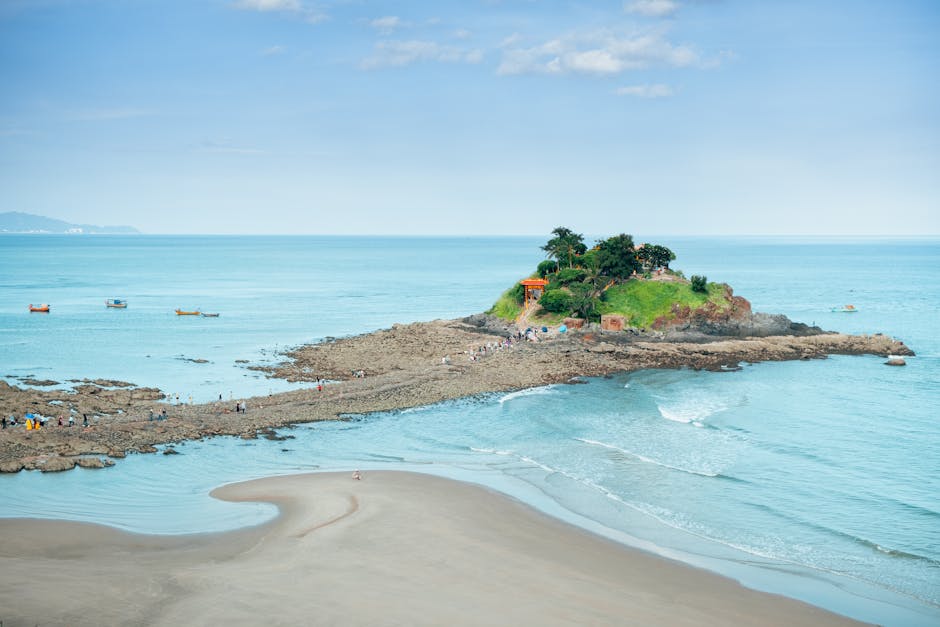 A picturesque view of Vũng Tàu beach with a small island and boats on a clear day in Vietnam.