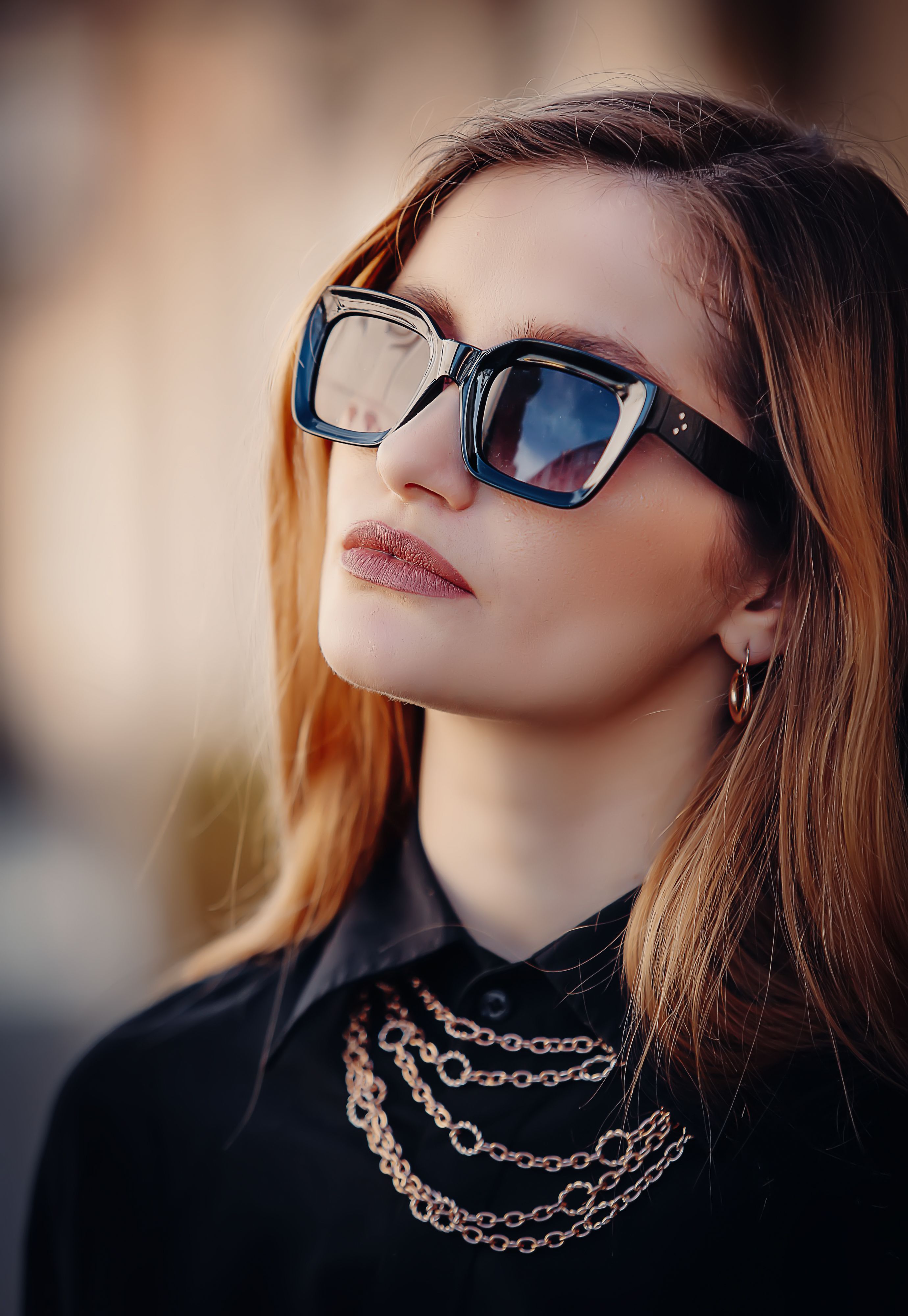 Stylish portrait of a woman with sunglasses and jewelry, captured outdoors in natural light.