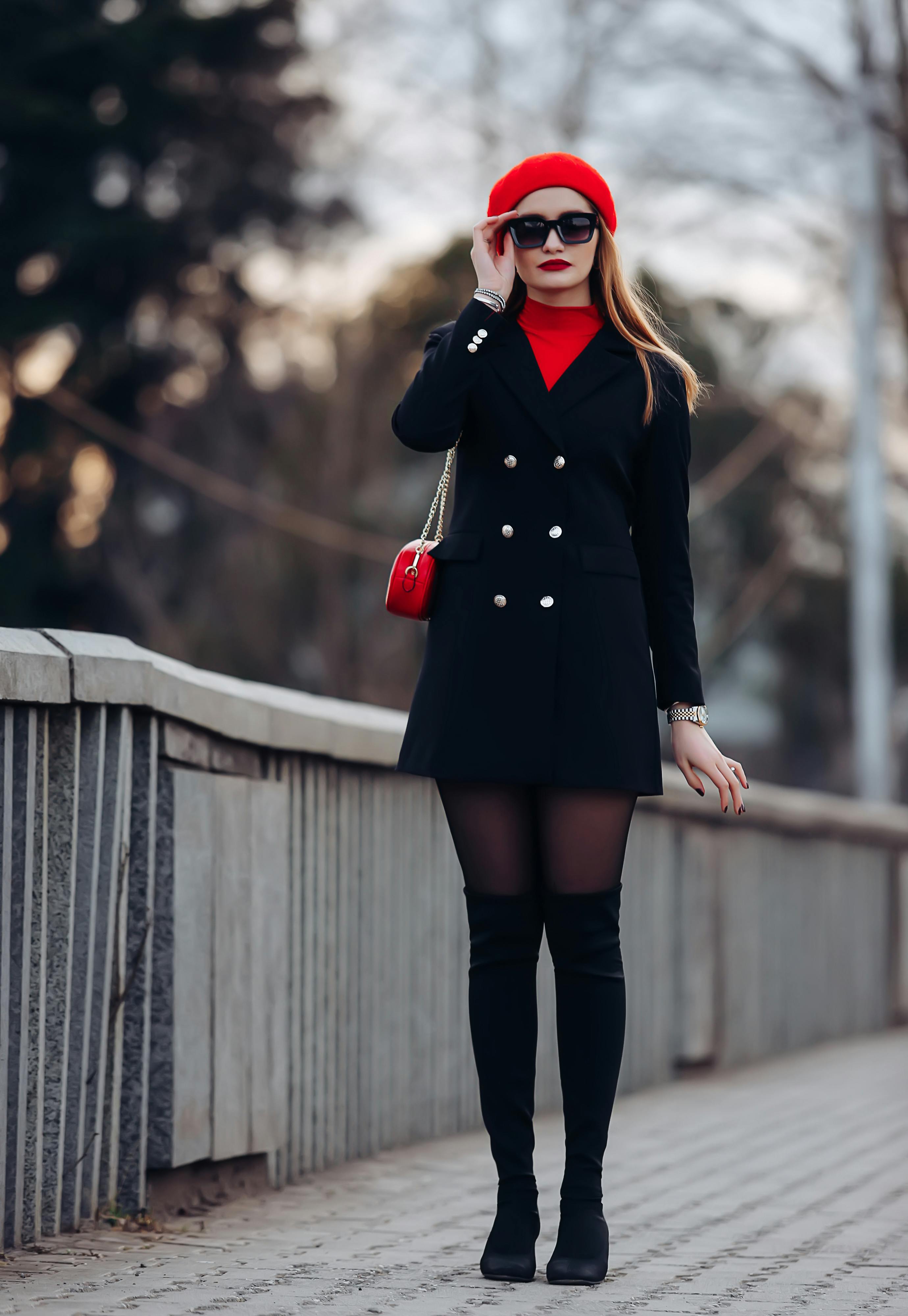 Free Elegant woman in a black coat and red beret poses stylishly on a city walkway. Stock Photo