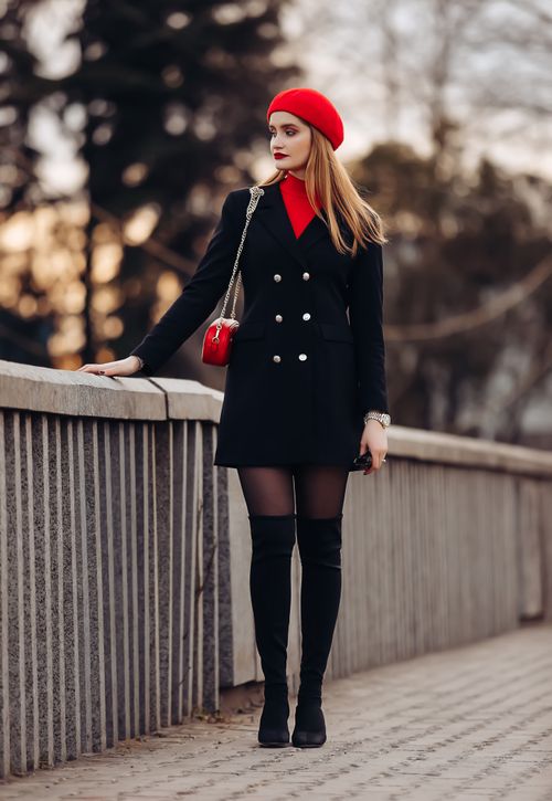 Free Stylish woman in black coat and red beret posing on a city bridge at sunset, showcasing elegance and fashion. Stock Photo