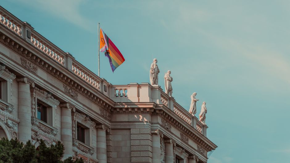 Arquitectura elegante con una bandera del orgullo y estatuas clásicas en la azotea.