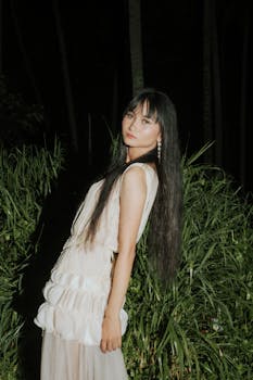 A woman in a stylish dress posing outdoors in a serene nighttime garden setting.