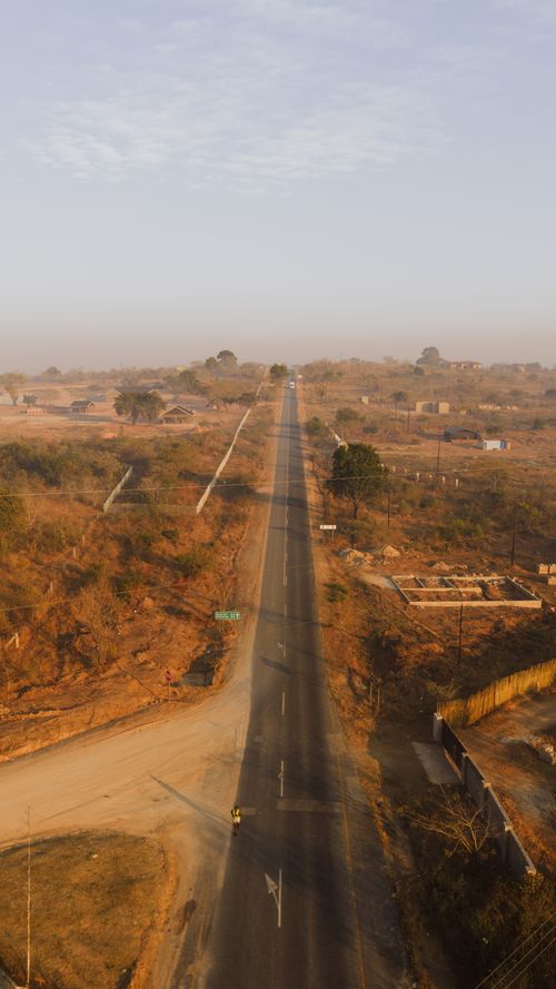 Free Drone photo capturing a straight rural road in Numbi, Mpumalanga, at sunrise, featuring an expansive landscape. Stock Photo