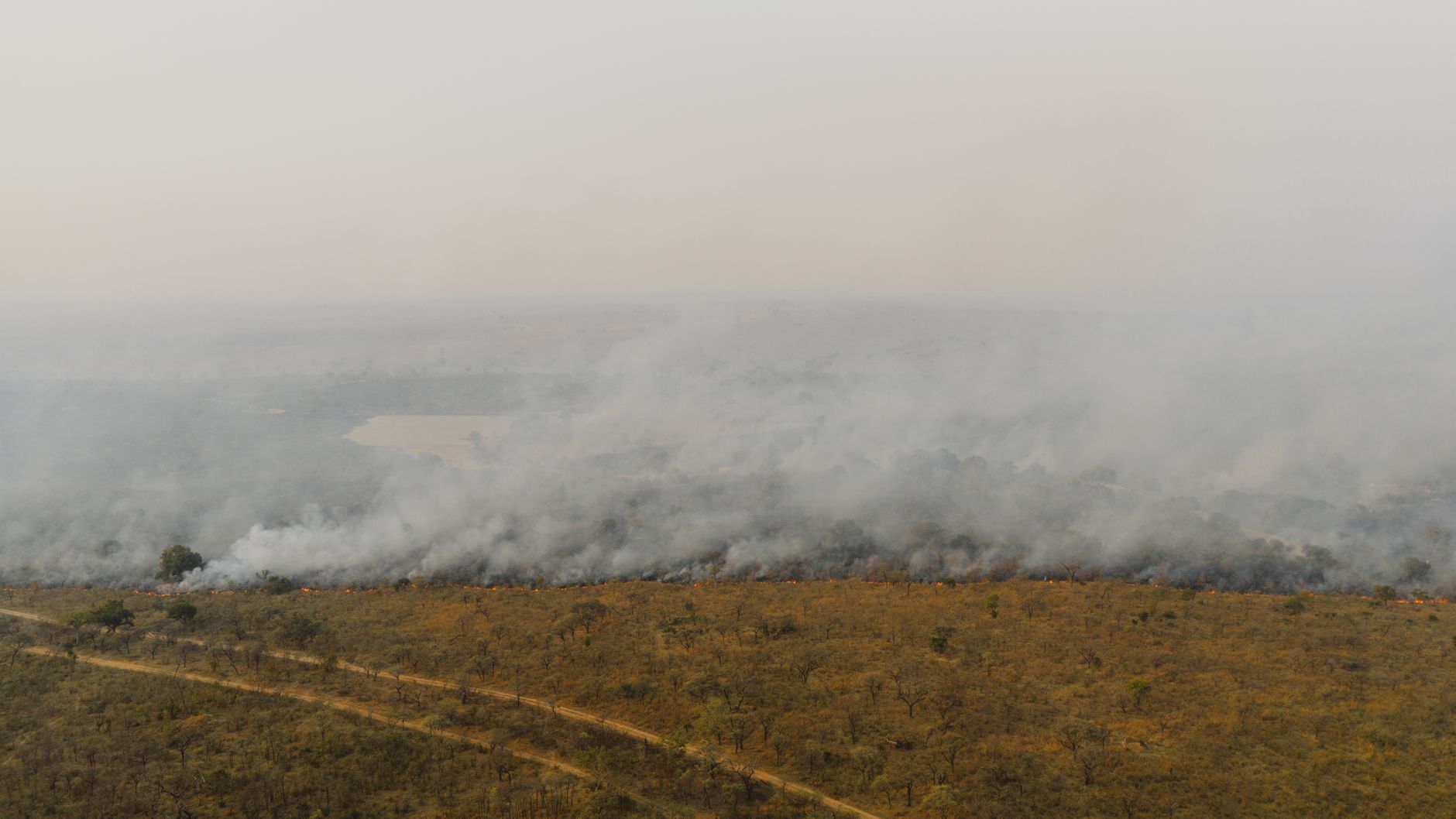 Aerial shot of a wildfire spreading through a South African grassland, producing smoke and haze.